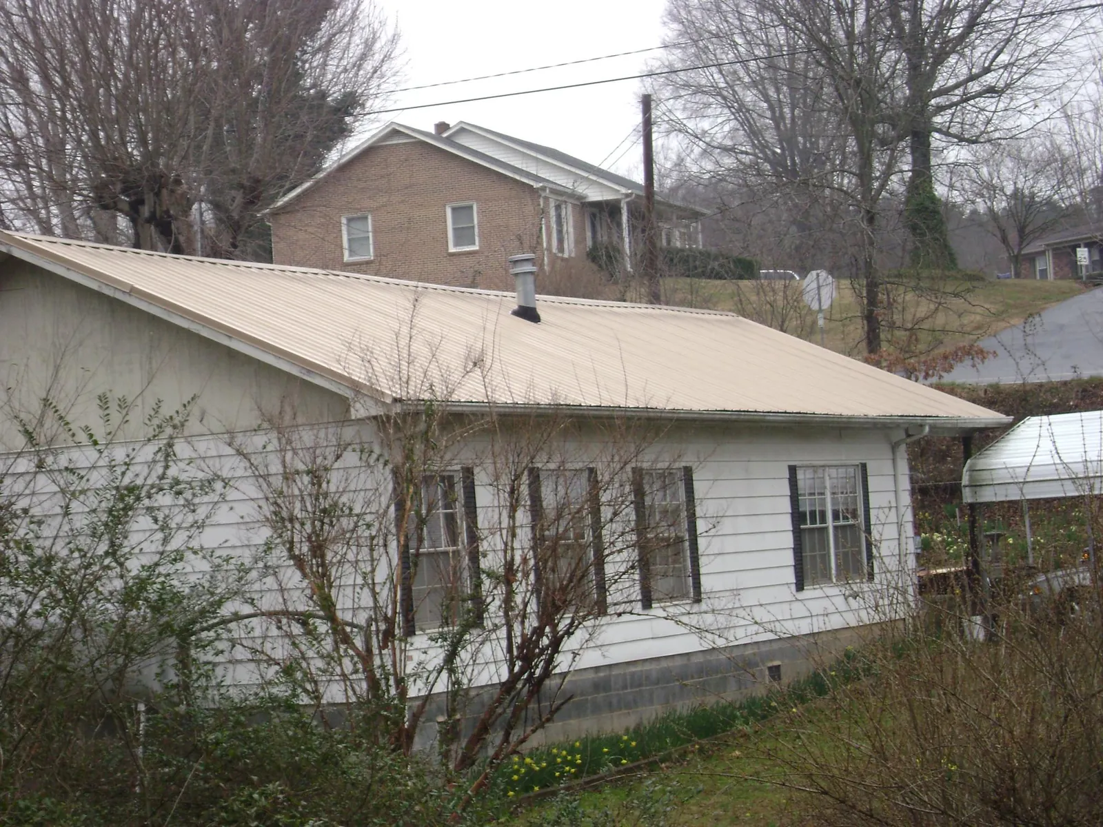Tan metal roof on a white sided house set into a hillside — Commercial Roofing by Roofing Brothers in Bridgeton